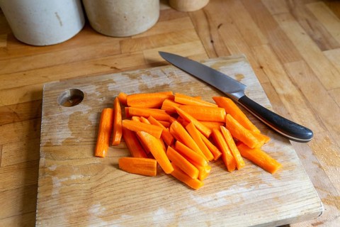 Sliced carrots on wooden chopping board with knife