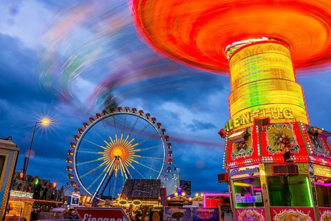 Illuminated chain carousel in motion, behind the Ferris wheel at standstill, Festwiese,