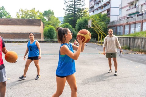 Concentrated female basketball player in blue uniform shooting ball during training outdoors on a