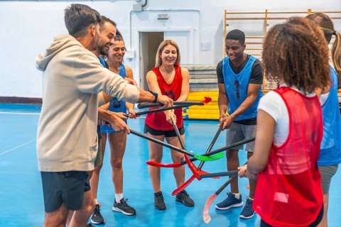 Floorball players gathering their sticks in a circle before a match, smiling and displaying