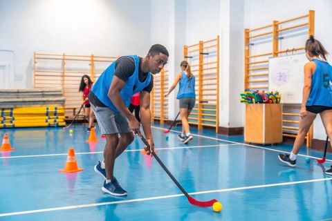 Focused young athlete dribbling floorball ball in gym, practicing stick handling skills with