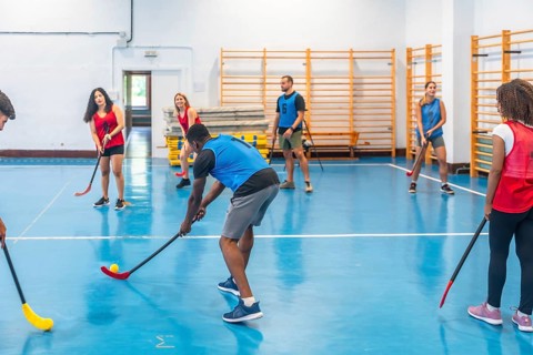 Floorball team players practicing passes during training inside a gym, skillfully hitting the ball