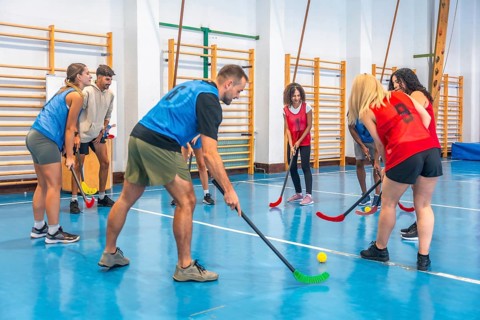 Two floorball teams wearing colorful sportswear are practicing passes and shots in a gymnasium,