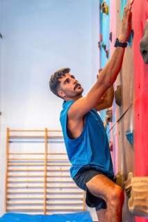 Concentrated male athlete meticulously gripping colorful handholds while ascending an artificial