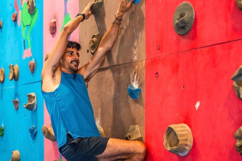 Focused male athlete ascends a vibrant indoor climbing wall, demonstrating strength, agility, and