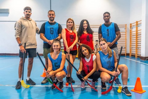 Multi ethnic floorball team posing together with their sticks in gymnasium after training session,