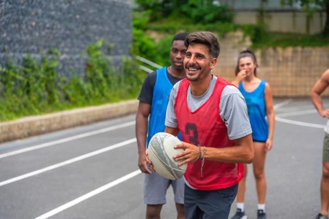 Rugby player wearing a red training bib smiling while holding the ball during a lively training