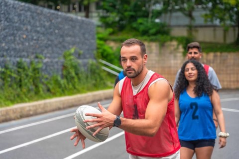 Male rugby player wearing red training bib holding and passing rugby ball on outdoor court during
