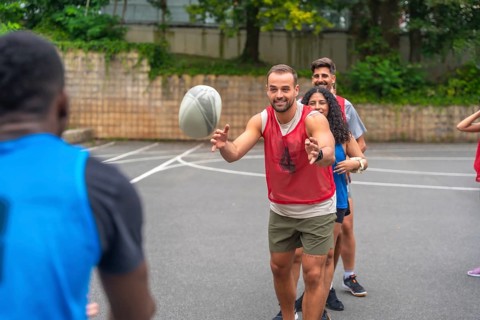 Group of athletes passing a rugby ball during a training session on an urban basketball court,
