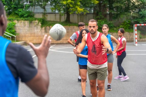 Multi ethnic rugby players engaging in passing drills on an outdoor court within a city park,