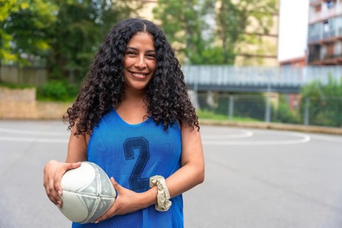 Young woman wearing a blue rugby uniform, confidently holding a rugby ball while smiling on an