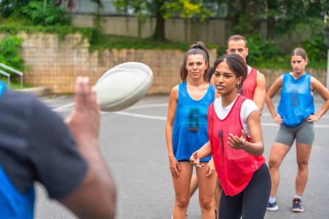 Coach throws a rugby ball to a group of female players wearing numbered jerseys during a training