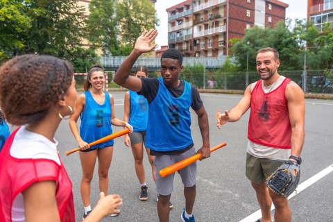 Group of cheerful multi ethnic friends wearing sportswear giving high fives and holding bats while