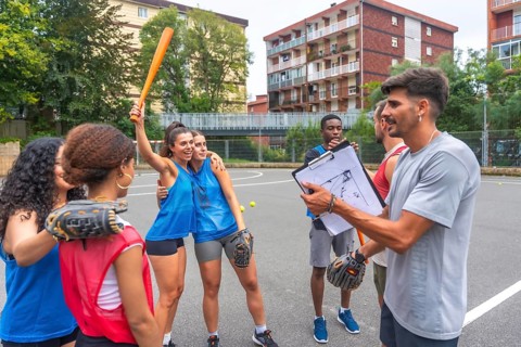 Female baseball players celebrating a victory with their coach holding a clipboard, discussing