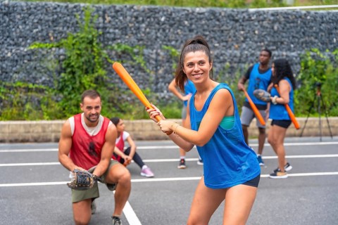 Smiling sportswoman holding an orange baseball bat, getting ready to hit the ball during a friendly