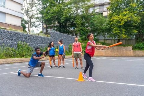 Group of friends enjoying a lively game of baseball on an outdoor court, with a woman swinging an