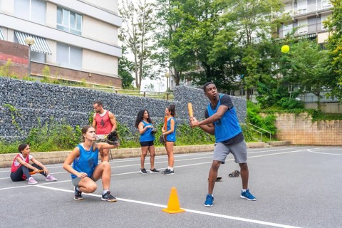 Group of young friends playing baseball in an urban environment, with a male player hitting the