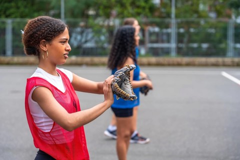 Young woman baseball player putting on her glove, preparing for practice with teammates under the