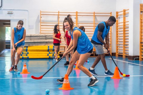 Female and male athletes wearing blue t shirts are practicing floorball, dribbling with sticks