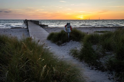 Evening beach dunes and lonely passenger pier at sunset, peaceful sea waves, Kobaek Strand,