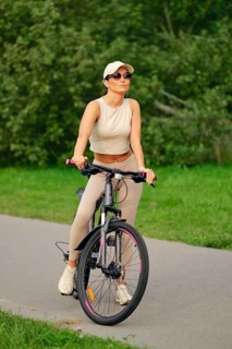 A woman enjoys a leisurely ride on her bicycle along a paved path in a vibrant green park. She