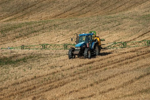 Tractor spreading fertilizer on harvested stubble field in Ystad municipality, Skåne county,