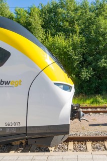 Front view of a train on the tracks, surrounded by green vegetation, battery Electric train with
