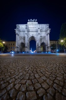 Night shot of the illuminated Siegestor on cobblestone street, Siegestor, Munich, Germany