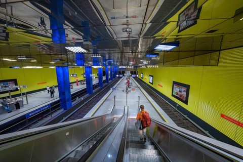 Modern underground station with yellow walls and escalator, people in the hall, Münchner Freiheit,
