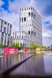 Futuristic high-rise building and park landscape under a blue sky with a colourful element, Munich,