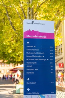 Urban signpost with various destinations, surrounded by trees under a sunny sky, Sindelfingen,