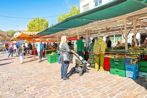 People stroll between market stalls with boxes full of goods under colourful umbrellas,