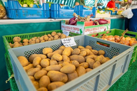 Market stall with crates full of potatoes and onions. Price label visible on one of the crates,
