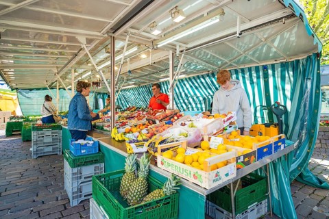 People buying fresh fruit at a colourful market stall under a striped market tent, Sindelfingen,
