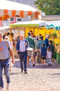 A busy outdoor market with lots of people and colourful stalls under parasols, Sindelfingen,