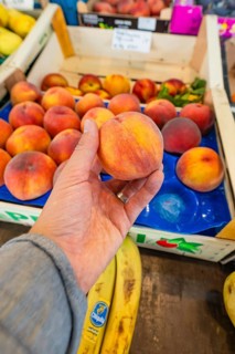 A hand holds a juicy peach over a crate of fresh fruit at a market stall, Sindelfingen, Böblingen