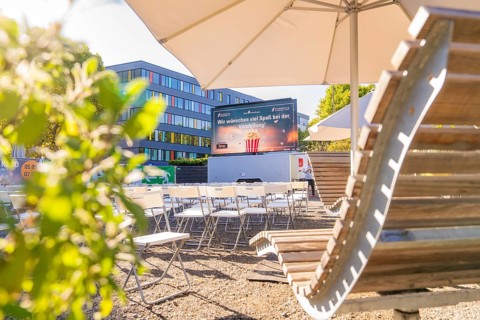 Rows of chairs under parasols in front of a screen, enlivened by sunshine, open air cinema