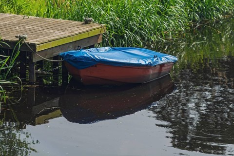 Red plastic boat with blue tarpaulin, Lower Saxony, Germany