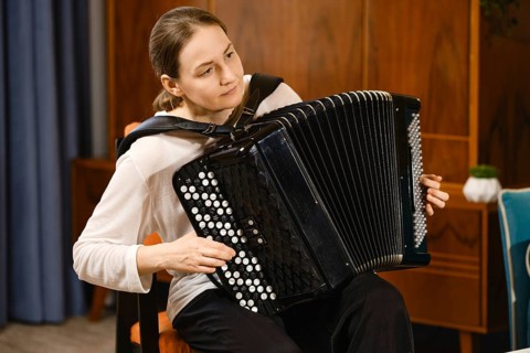 A middle-aged woman concentrates as she plays the accordion in a warmly decorated room, creating a