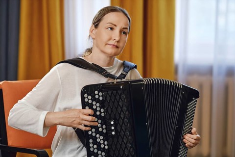 A woman sits comfortably in a chair, skillfully playing the accordion in a well-lit room adorned