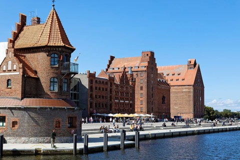 Visitors strolling and sitting on the waterfront promenade, building on the left two-storey brick