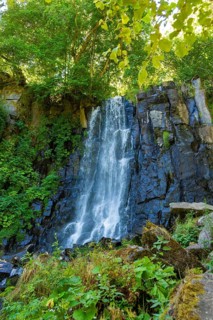 Vaucoux waterfall cascades gracefully over dark rocks, surrounded by lush greenery, Auvergne