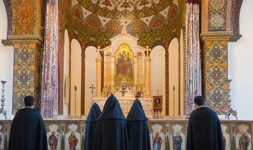 Many monks stand in front of an elaborately decorated altar with bright ornaments, Inside the