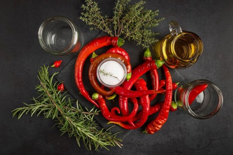 Hot red peppers with vinegar, oil, salt and herbs on a black background