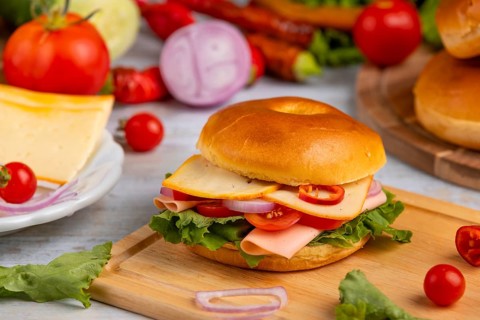 A bagel topped with cheese, sausage, tomatoes, onion and lettuce leaves on a wooden board