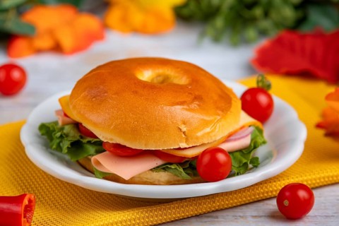 A filled bagel on a plate, decorated with tomatoes on a yellow cloth
