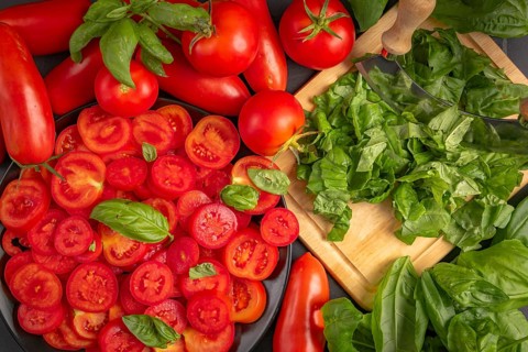 Fresh tomatoes and basil leaves on a chopping board, in bright red and green colours