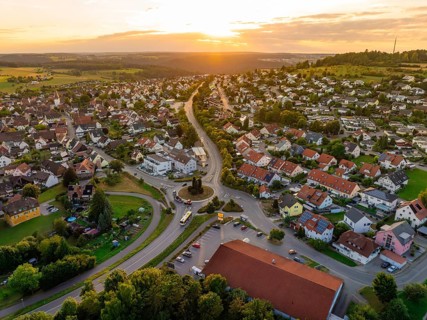 Sea of houses with curved streets in warm sunset light and green surroundings, small town of Perle