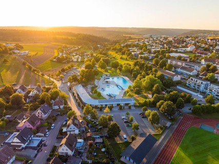 Aerial view of a village with swimming pool and surrounding houses at sunset, small town of Perle