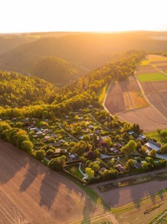 Campsite nestled between fields and wooded hills in the warm sunset light, small town of Perle